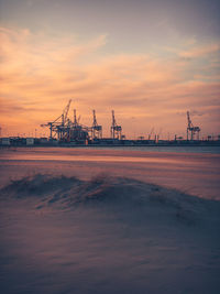 Cranes on pier by sea against sky during sunset