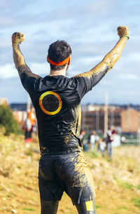 Participant in extreme obstacle race cheering, rear view