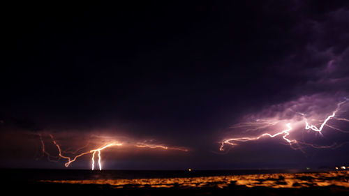 Lightning over illuminated cityscape against sky at night