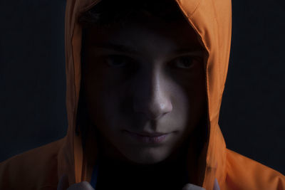 Close-up portrait of young woman in hooded shirt against black background