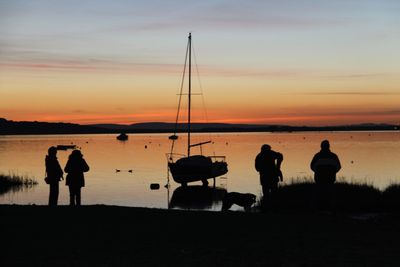 Silhouette people on shore against sky during sunset