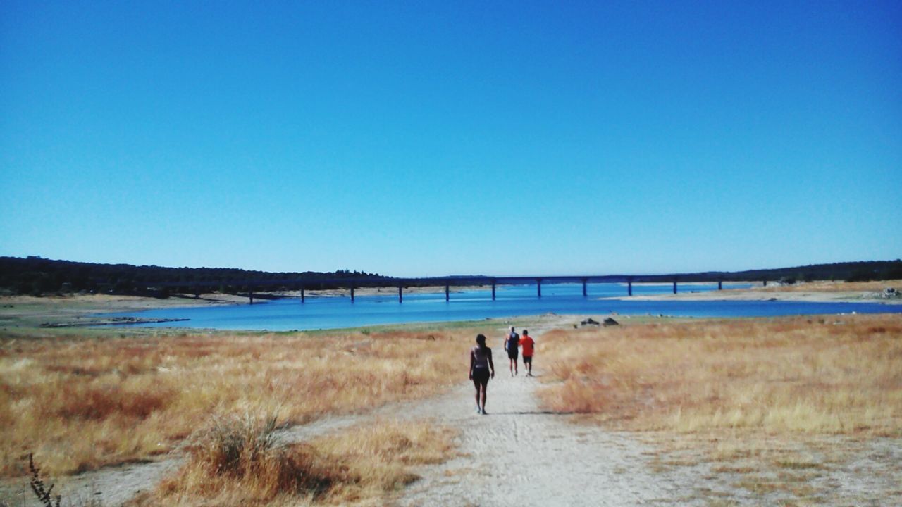 water, blue, clear sky, grass, copy space, tranquil scene, lake, tranquility, scenics, day, beauty in nature, nature, calm, person, vacations, remote, lakeside, non-urban scene, solitude, outdoors, countryside, tourism