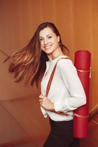 Portrait of smiling woman with exercise mat standing at home