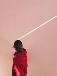 Rear view of woman in red hooded shirt by wall
