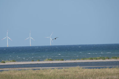 Wind turbines on sea against clear sky