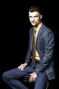 Portrait of young man sitting against black background