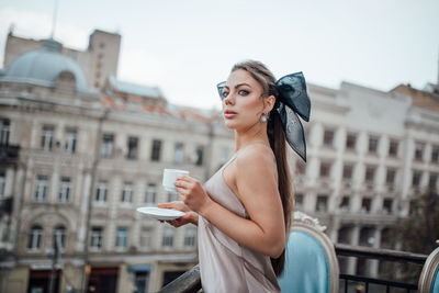 Portrait of beautiful woman standing against buildings in city