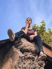 Low angle view of young woman sitting on rock