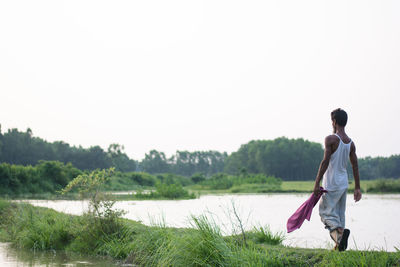 Rear view of man standing by lake against sky