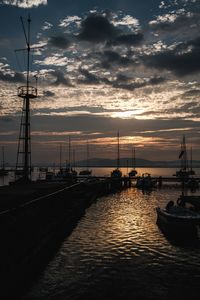 Sailboats moored in harbor at sunset