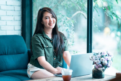 Portrait of young woman using mobile phone while sitting at home