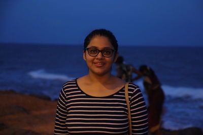 Portrait of smiling young woman standing at beach against sky