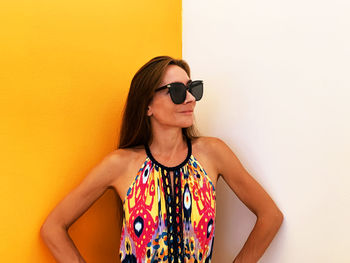 Portrait of young woman wearing sunglasses standing against wall