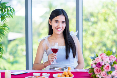 Smiling young woman holding drink in glass at table