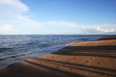 The view on a beach with sea, blue sky and white sand on a sunny day.