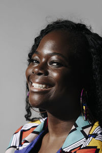 Happy african american woman with curly hair smiling and looking at camera while standing against gray background