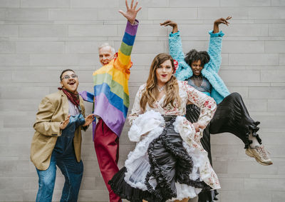 Portrait of happy fashionable friends gesturing against wall