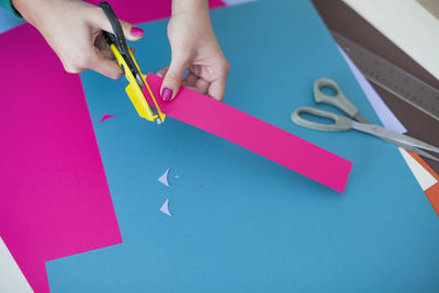 Cropped hands of woman cutting pink kraft paper on table