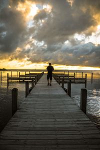 Rear view of man on pier over sea against sky during sunset