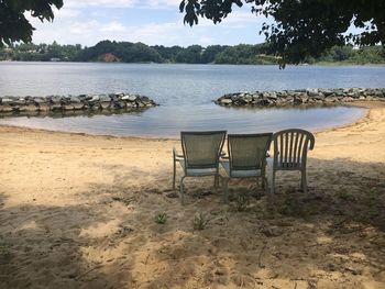 Empty chairs on beach against sky