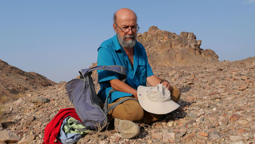Portrait of senior man sitting on mountain against clear sky