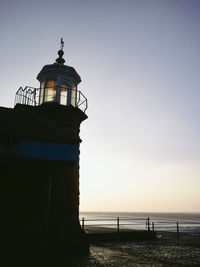 Lighthouse by sea against clear sky