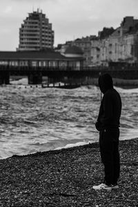 Rear view of man standing at beach against buildings in city