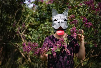 Midsection of man wearing french bulldog origami mask holding purple lilac flowering plants