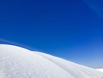 Snow covered land against clear blue sky