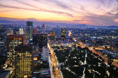 Aerial view of illuminated city buildings against sky during sunset