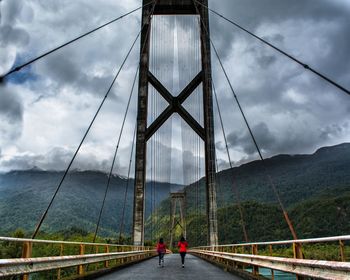 Rear view of people walking on suspension bridge against sky