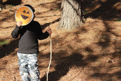 Boy holding art on paper over face while standing in forest