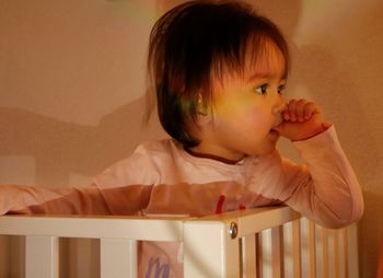 Close-up of cute girl sucking thumb while sitting in crib at home