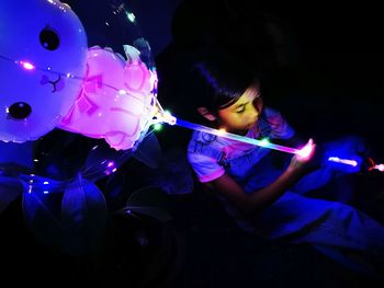 Cropped hand of young woman holding illuminated string lights at night