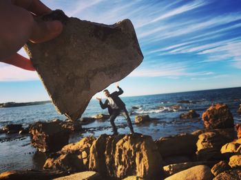 Close-up of man holding rock at beach against sky