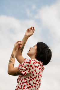 Low angle view of woman with tattoo on hands against sky