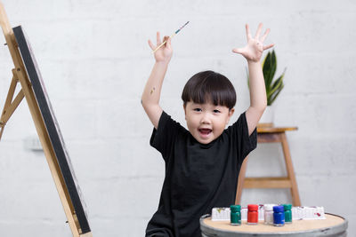 Portrait of boy holding paintbrush against wall