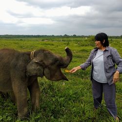 Full length of woman feeding elephant on field against sky