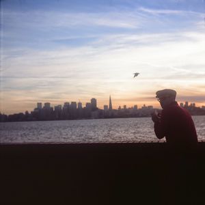 Rear view of man standing by retaining wall against sky during sunset