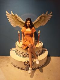 Portrait of woman sitting on artificial cake with wings