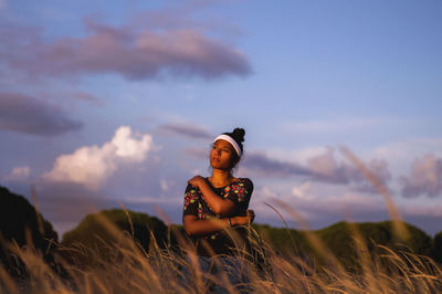 Woman sitting on field against sky during sunset