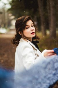 Portrait of beautiful young woman holding scarf standing in forest