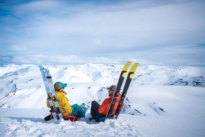 Woman and man sitting against skis with mountains in background