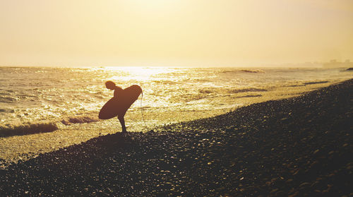 Silhouette woman walking at beach against sky during sunset