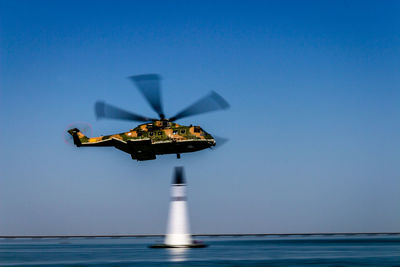 Helicopter over distance marker in sea against clear blue sky