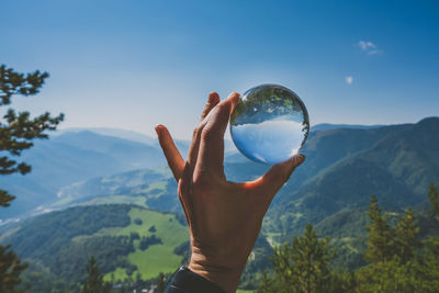 Cropped hand holding crystal ball against mountains