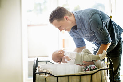 Father putting baby girl in cradle at home