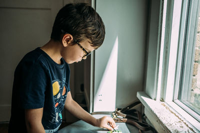Side view of boy looking through window at home