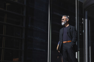 Businessman with hand in pocket looking away in city