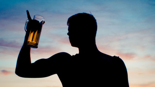 Low angle view of silhouette man holding beer glass against sky